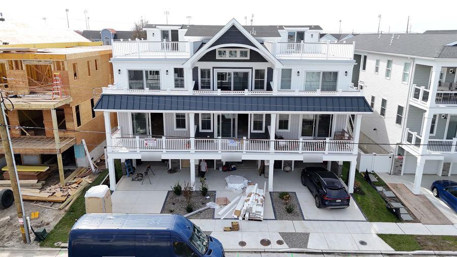 Front of a white home in Wildwood with a standing-seam porch roof and balconies, nearing completion